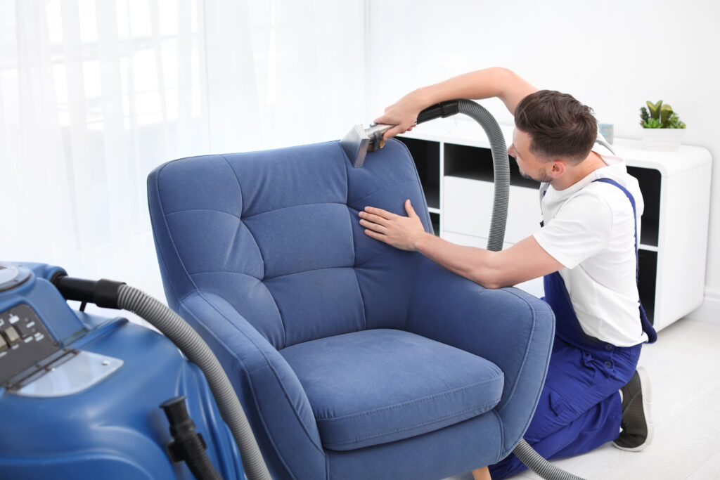 Dry cleaning worker removing dirt from armchair indoors