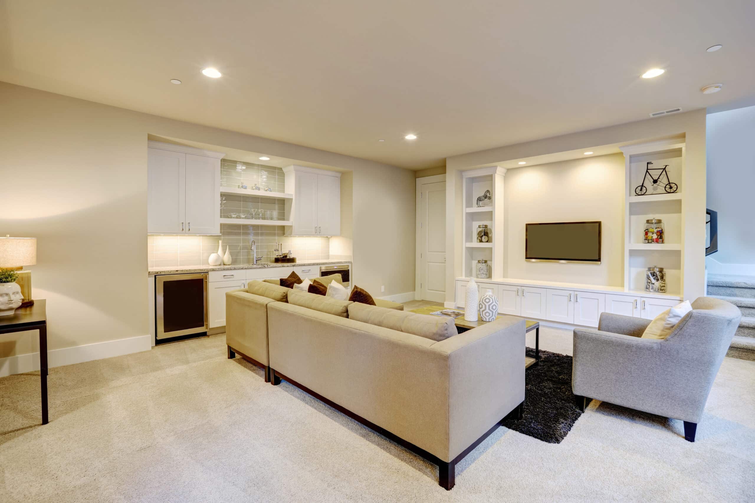 An elegant living room features a gray sectional facing a white built-in tv cabinet and wet bar mounted to a wall.